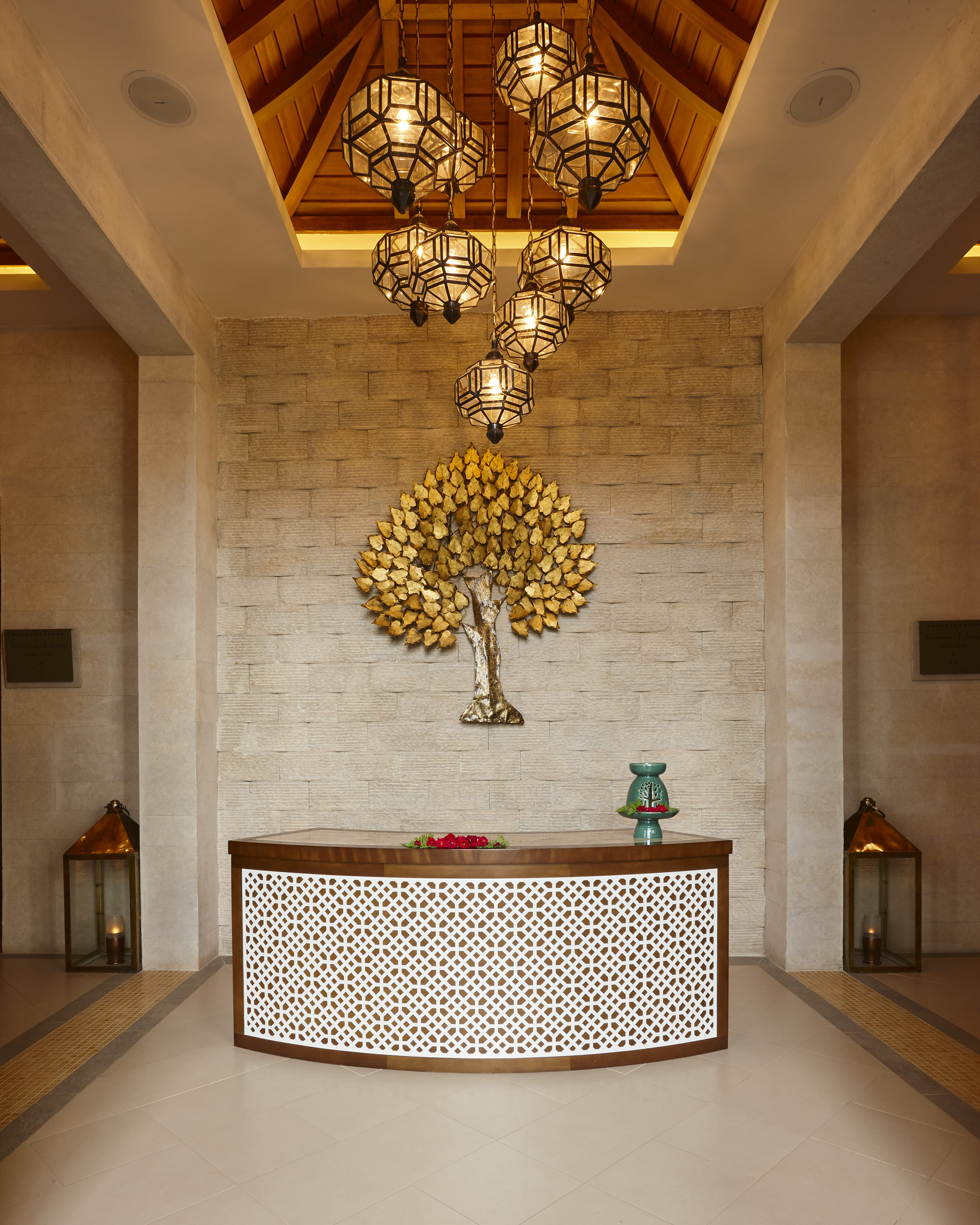 Rainforest Spa reception desk at Banyan Tree Tamouda Bay adorned with hanging lanterns and a golden tree decor.